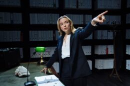 Actress Jodie Comer points off screen against a backdrop of law files