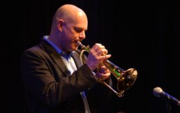 Jazz musician Damon Brown plays the trumpet against a black backdrop