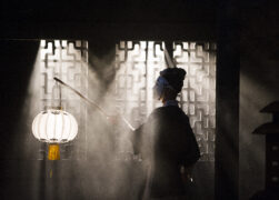 A masked opera singer holds a round, ornate Chinese lantern