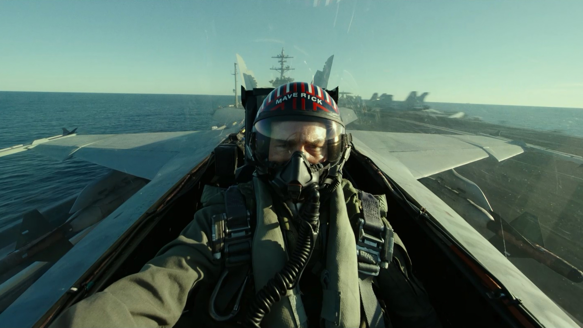 Actor Tom Cruise sits in a fighter jet as the pilot, wearing a blue and red helmet