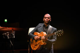 Musician Edison Herbert plays a guitar against a black backdrop