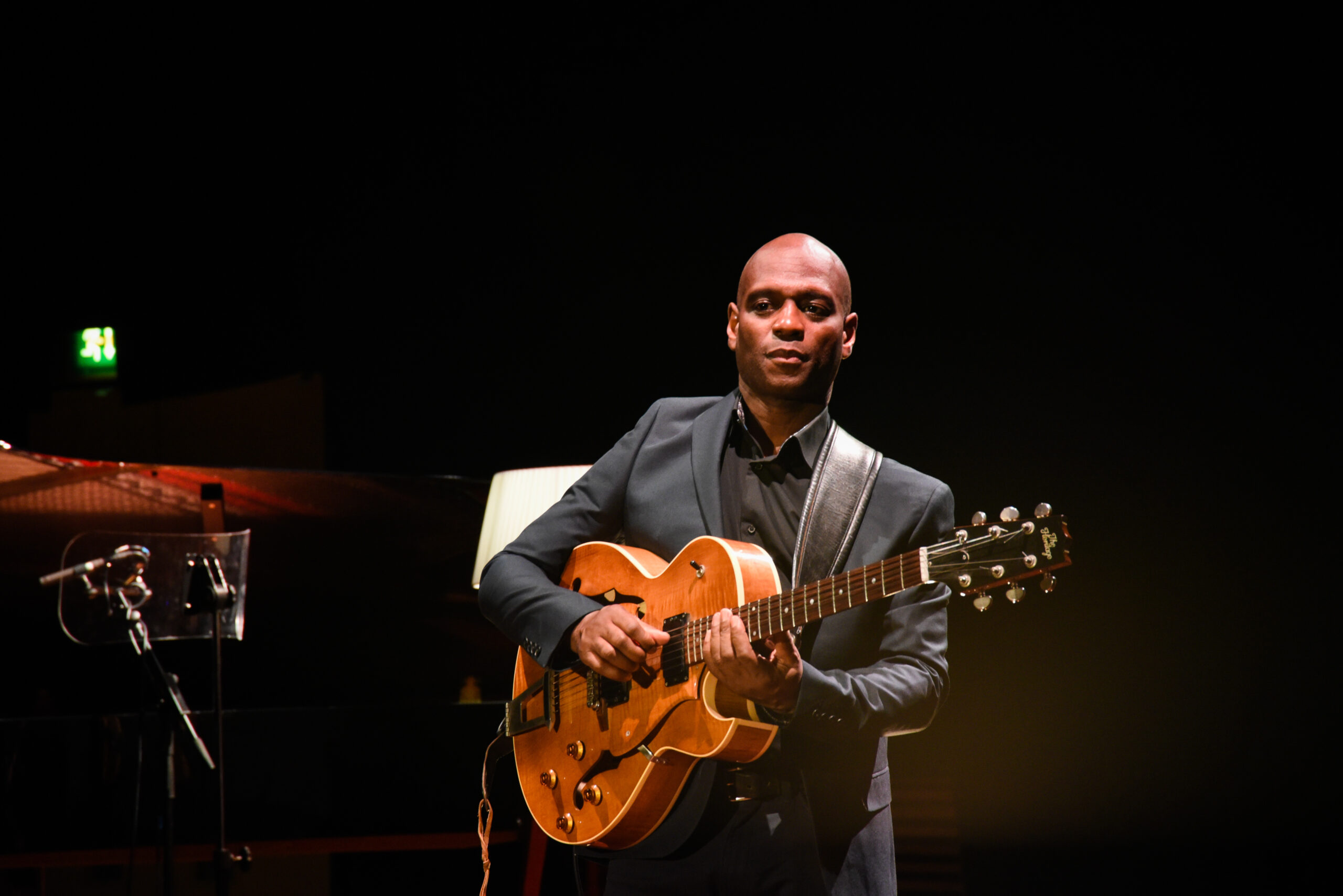 Musician Edison Herbert plays a guitar against a black backdrop