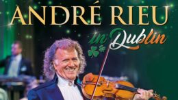 Classical musician Andre Rieu performs on with his signature violin against a background of green and orange