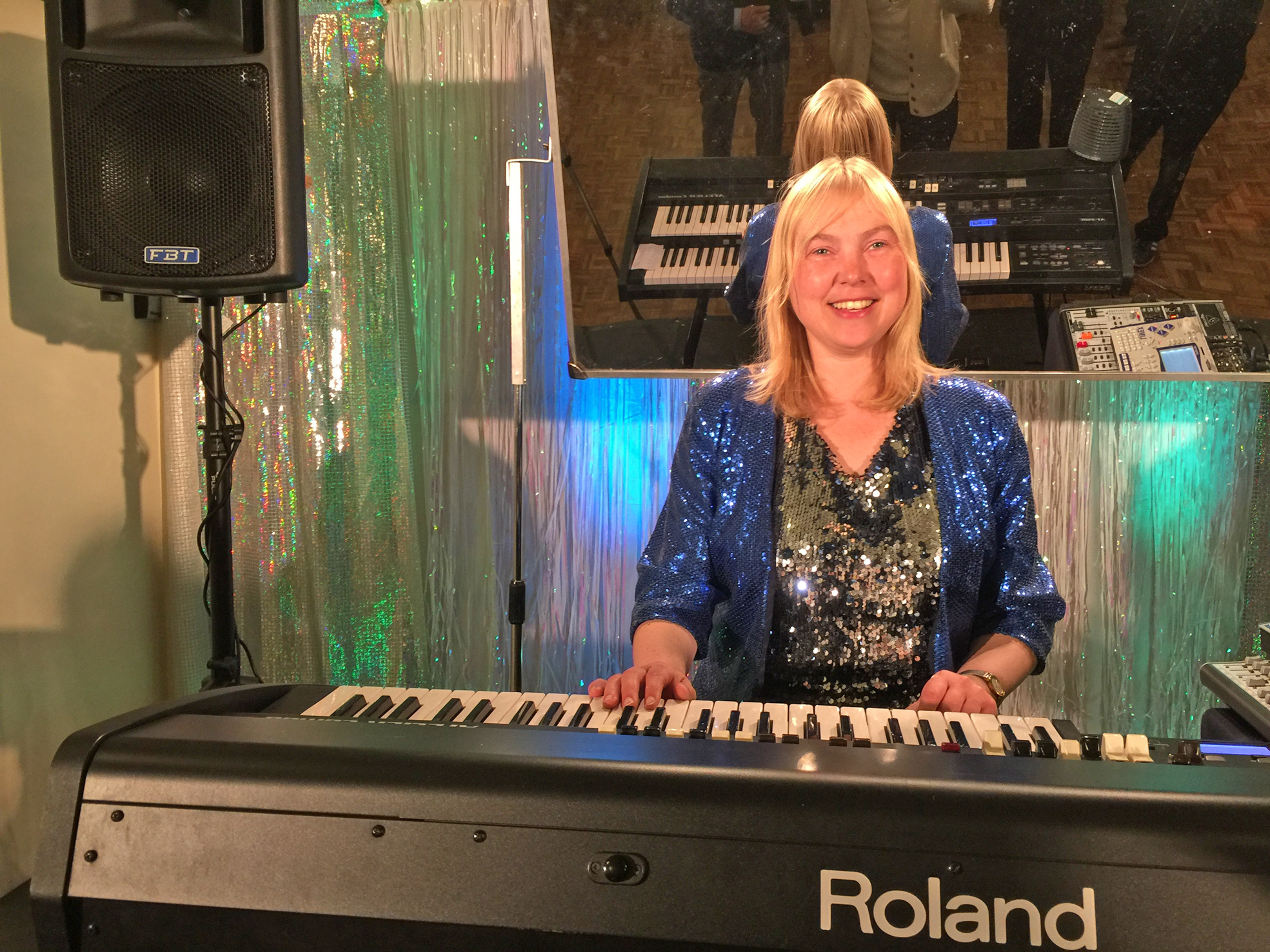 Organist Elizabeth Harrison sits behind an electronic keyboard in a glittery blue top, with blonde hair