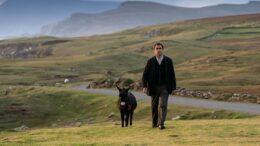 Actor Colin Farrell walks alongside a donkey in a rural setting