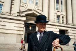 Actor Bill Nighy looks at his watch, dressed in a pinstripe suit and a bowler hat