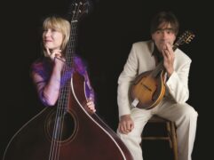 Musicians Hilary James and Simon Mayor pose against a black background with their instruments